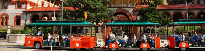 A train with people on it is going down a street in front of a building.