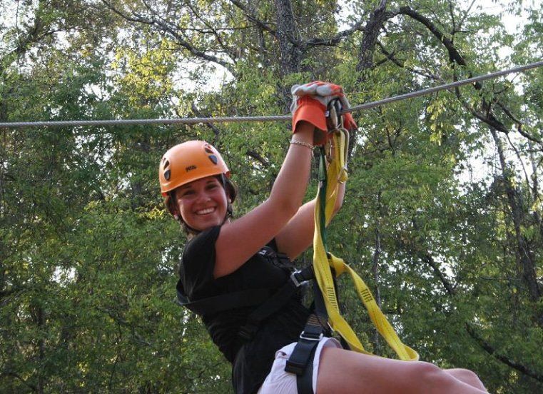 A woman wearing an orange helmet is riding a zip line