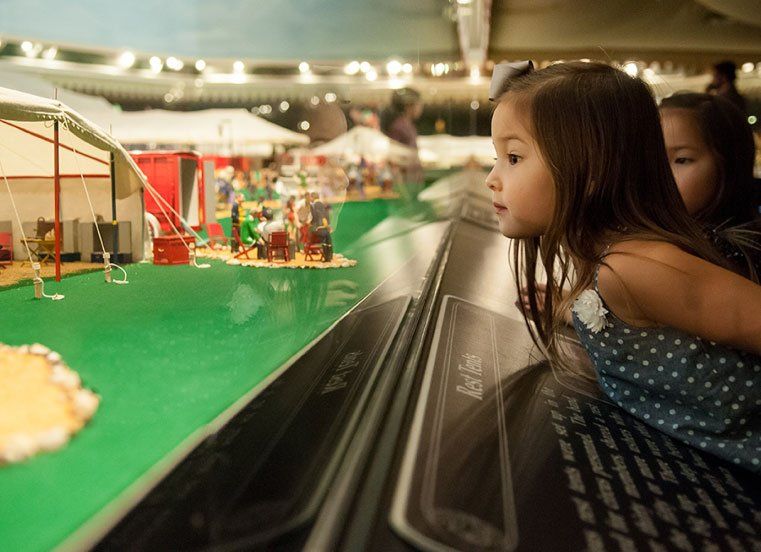 A little girl is looking at a model of a circus.