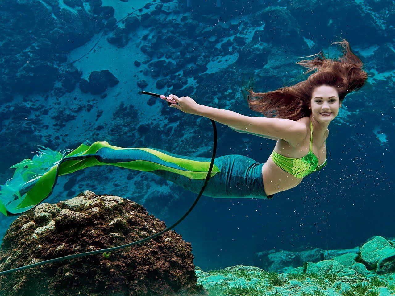 A woman in a mermaid costume is swimming in the ocean.
