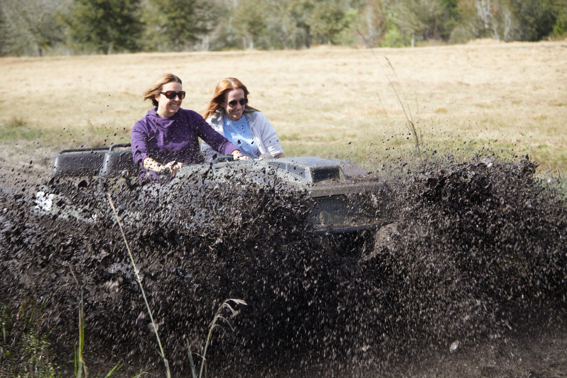Two women are driving a vehicle through a muddy field.