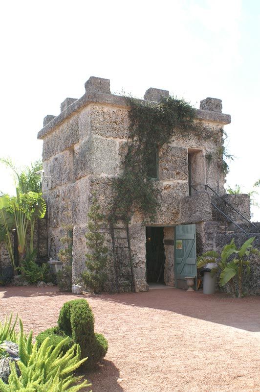 A small stone building with a blue door is surrounded by plants and bushes.