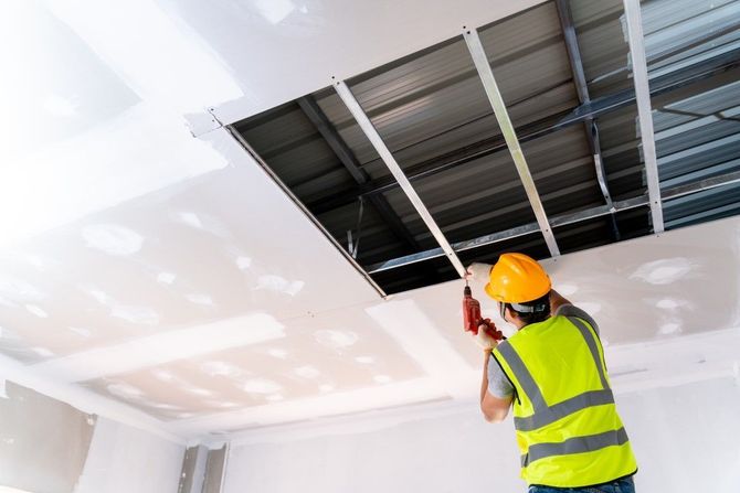 Worker in orange hard hat inspecting ceiling ductwork in a white room