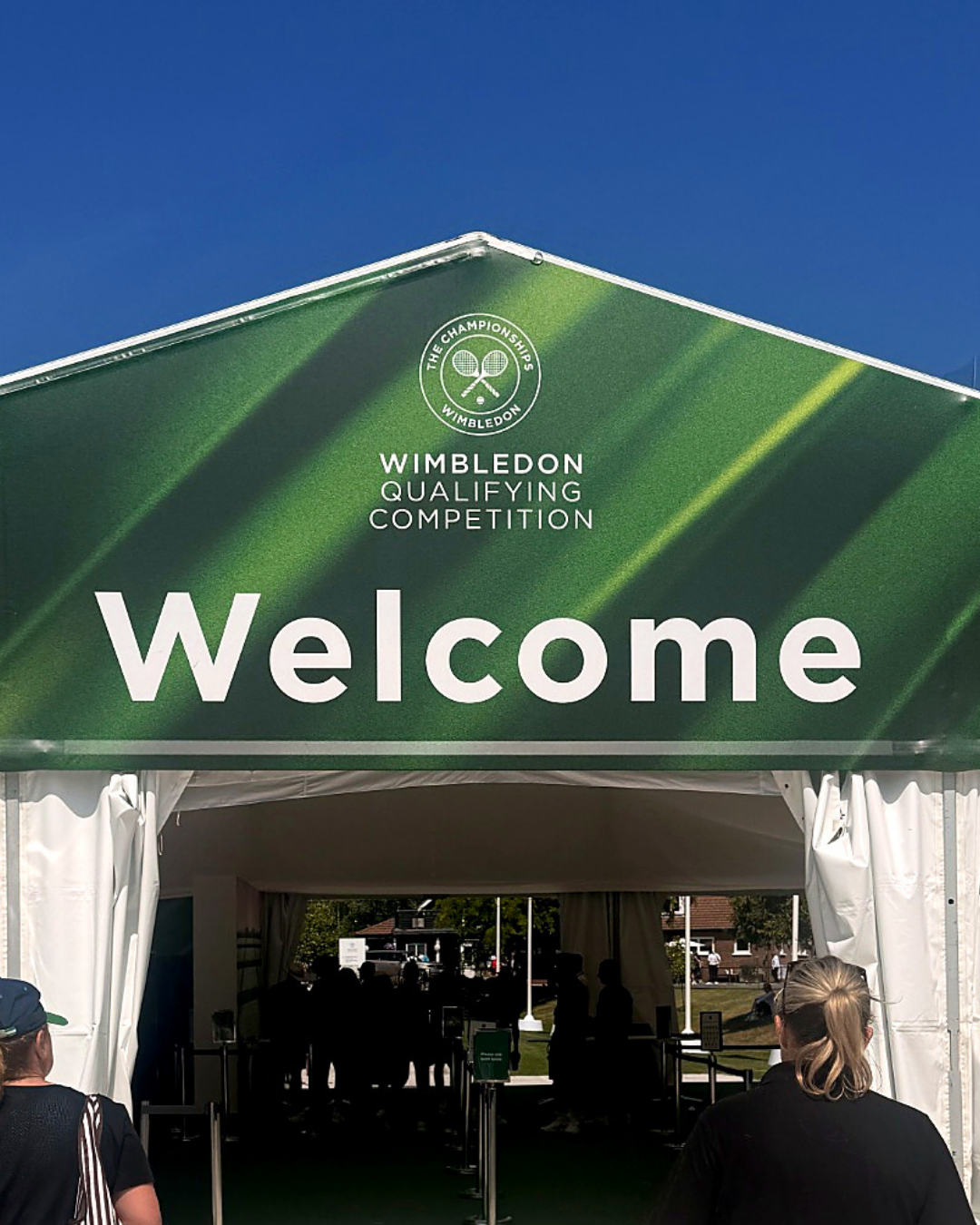 Wimbledon Championships welcome tent with green sign and people entering under a blue sky