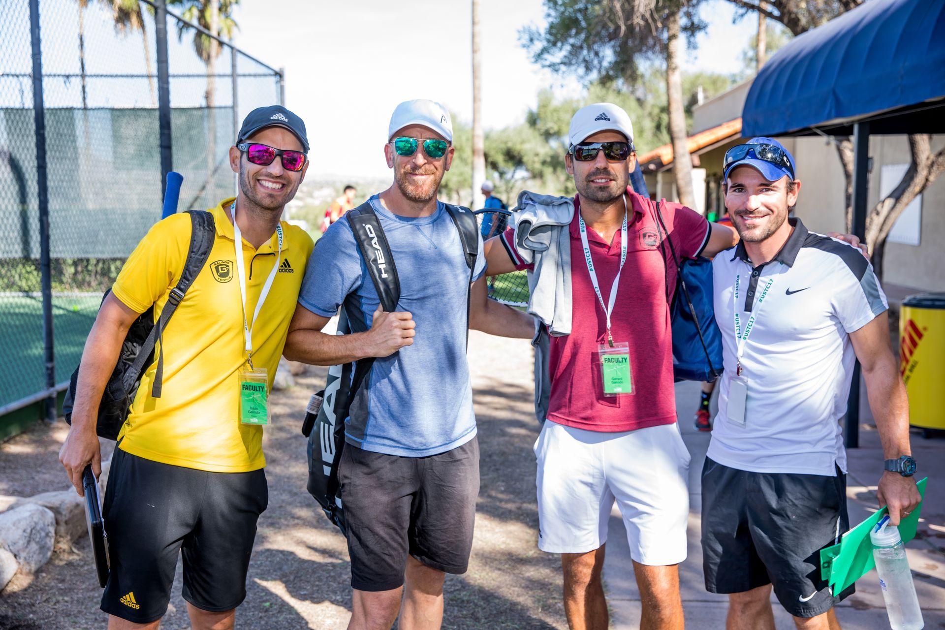 Five people posing outdoors in athletic gear, smiling and holding up drinks and bags.