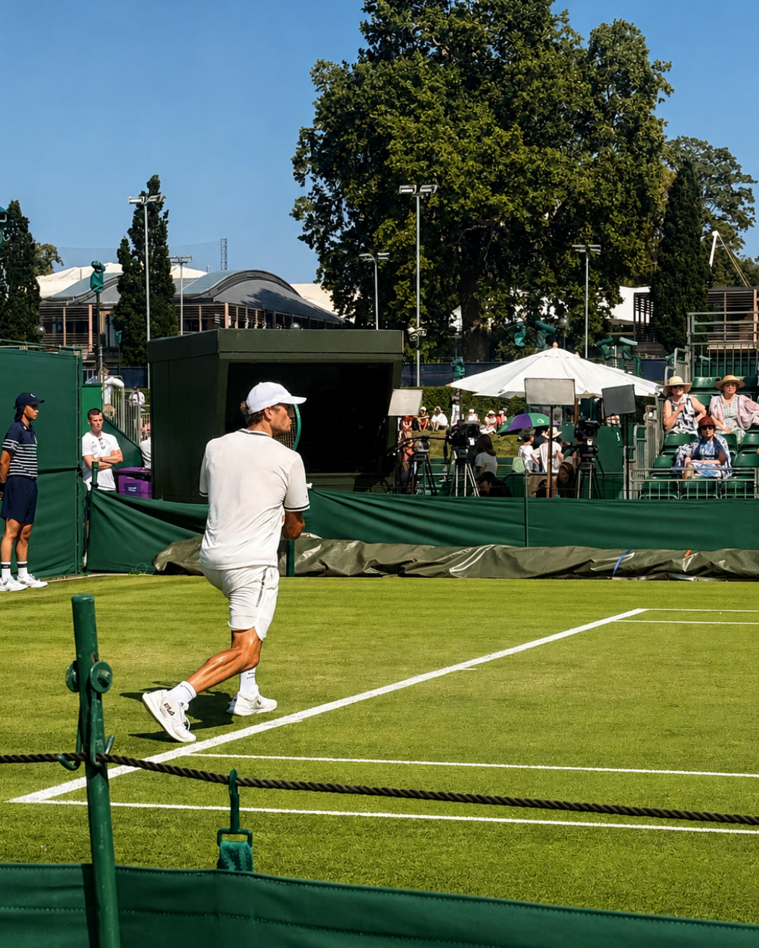 Tennis player in white serves on a grass court during an outdoor match in during Wimbledon Qualifying Rounds