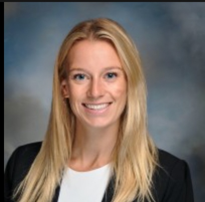Woman with long blonde hair smiles, wearing a black blazer over a white top, against a blue and grey blurred background.