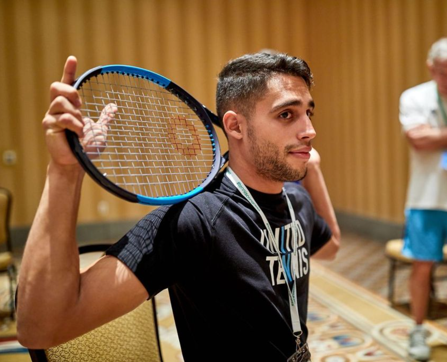 Tennis player with racket over shoulder, looking to the side. Wearing black shirt, indoors.