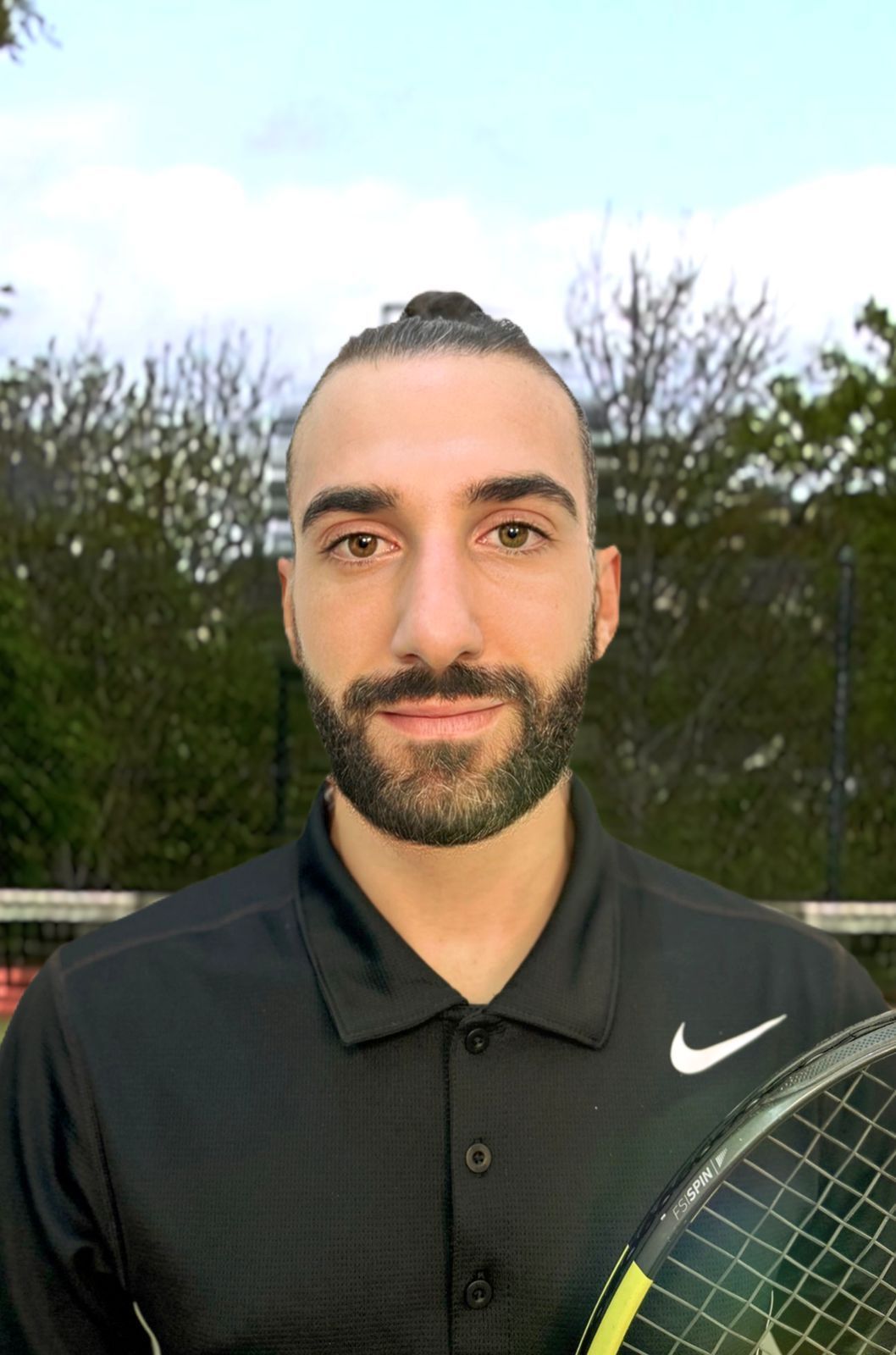 Man with beard holding tennis racket, wearing black shirt with a white Nike logo.