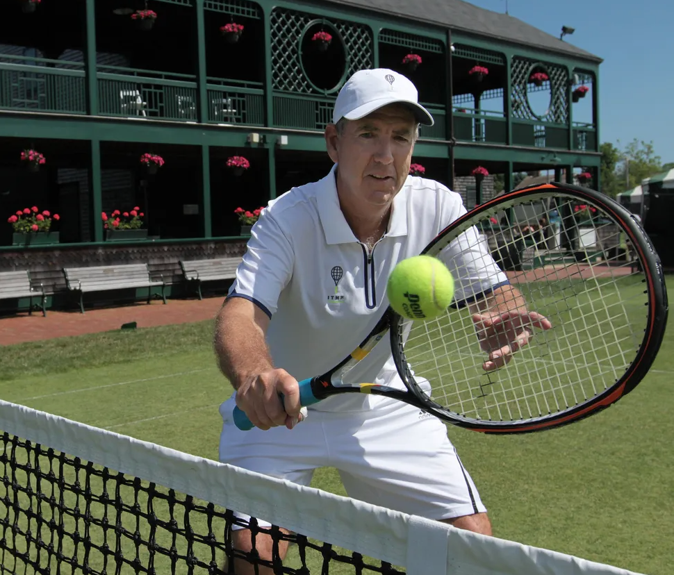 Man in white tennis attire hitting a yellow tennis ball with a racket on a grass court.