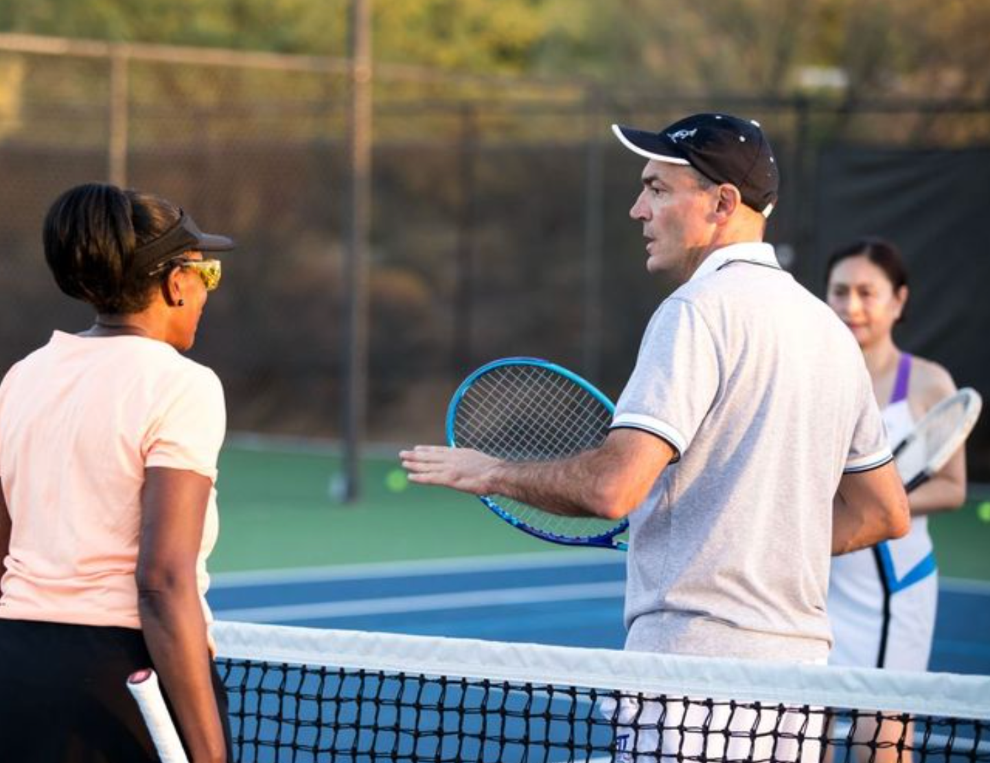 Tennis coach talking to a player on the court, another player nearby.