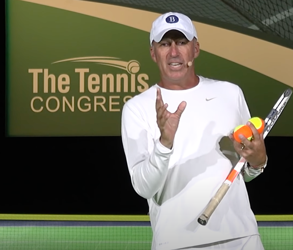 Man in white outfit holding tennis racket and balls, gesturing.