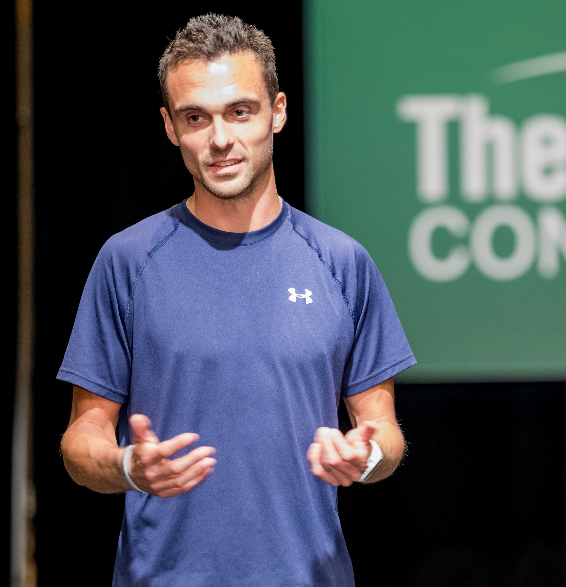 Man in blue shirt gesturing onstage with 
