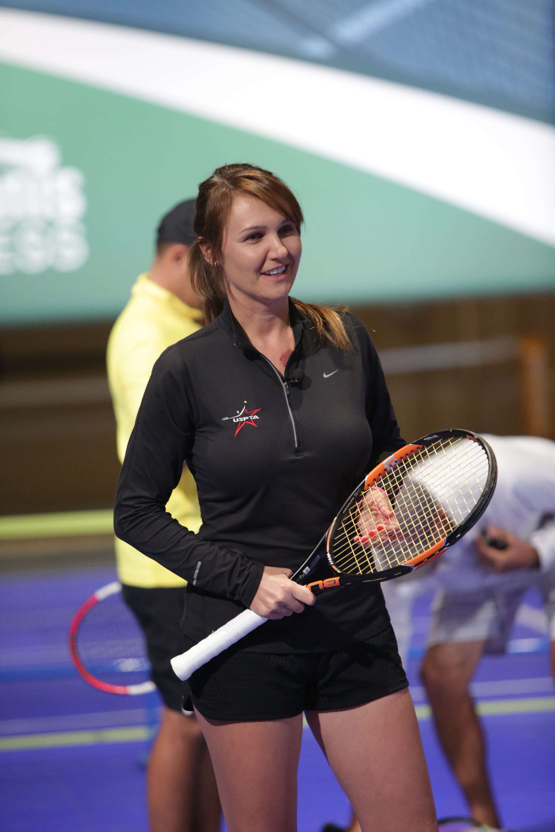 Woman in black athletic wear holding a tennis racket, smiling, standing on a court.