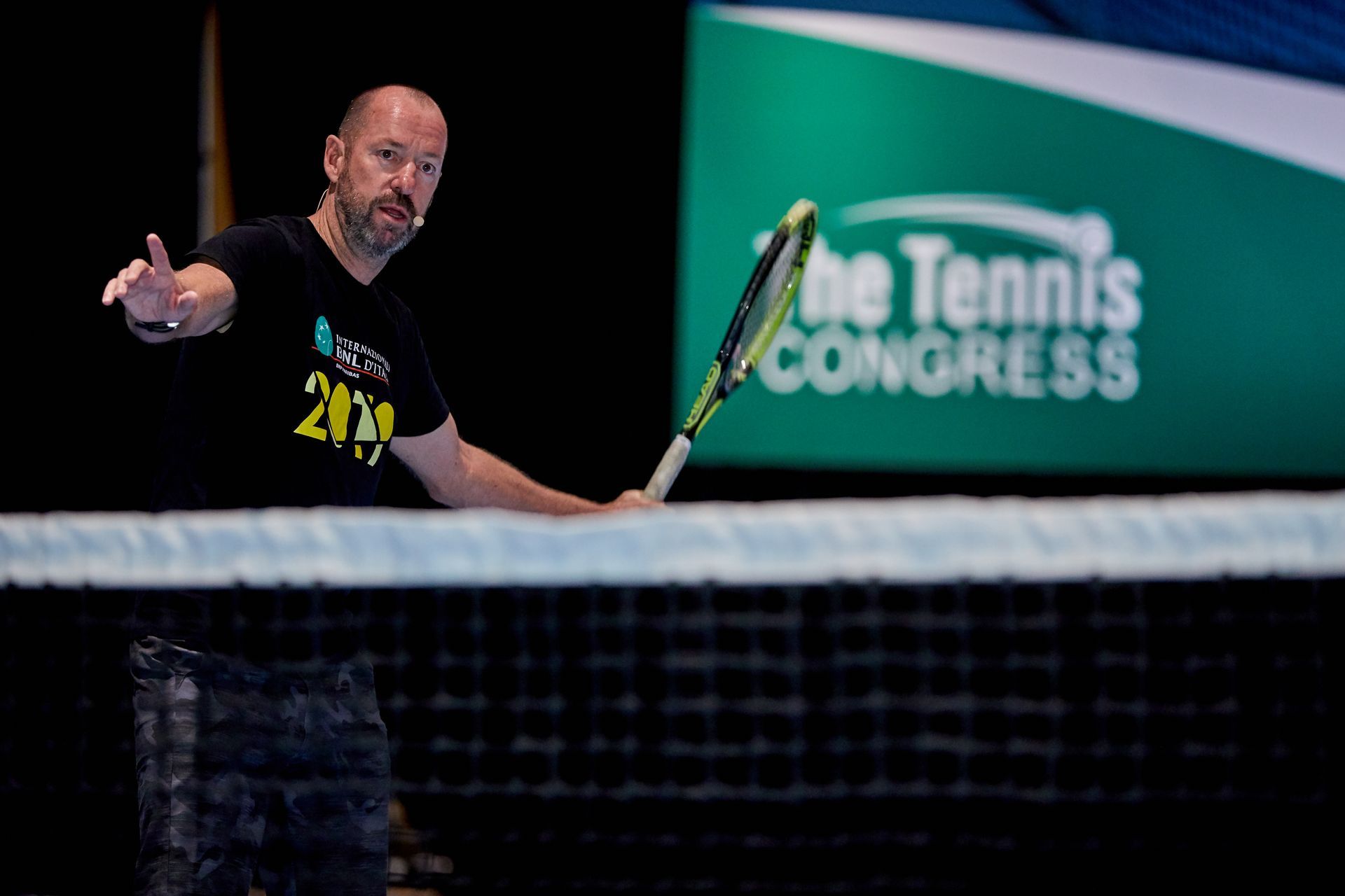 Man holding a tennis racket, gesturing near a net with 