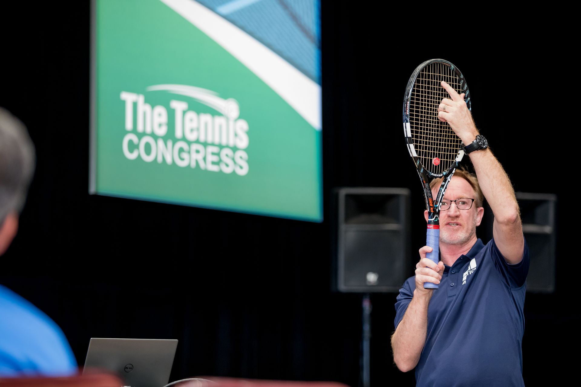 Man holding a tennis racket, presenting at 