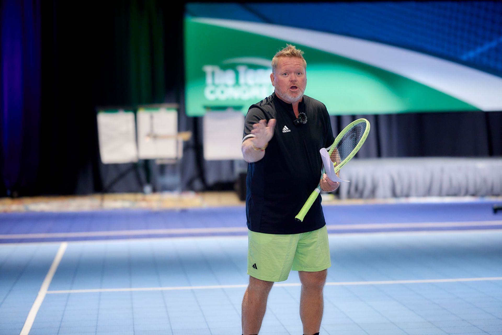 Man in black shirt and lime green shorts with a tennis racket, gesturing on a tennis court.
