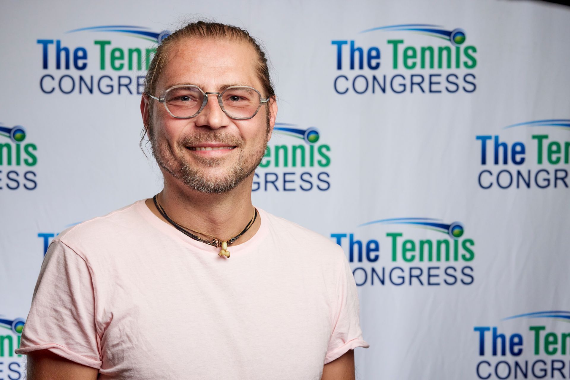 Man with glasses smiles, standing in front of 