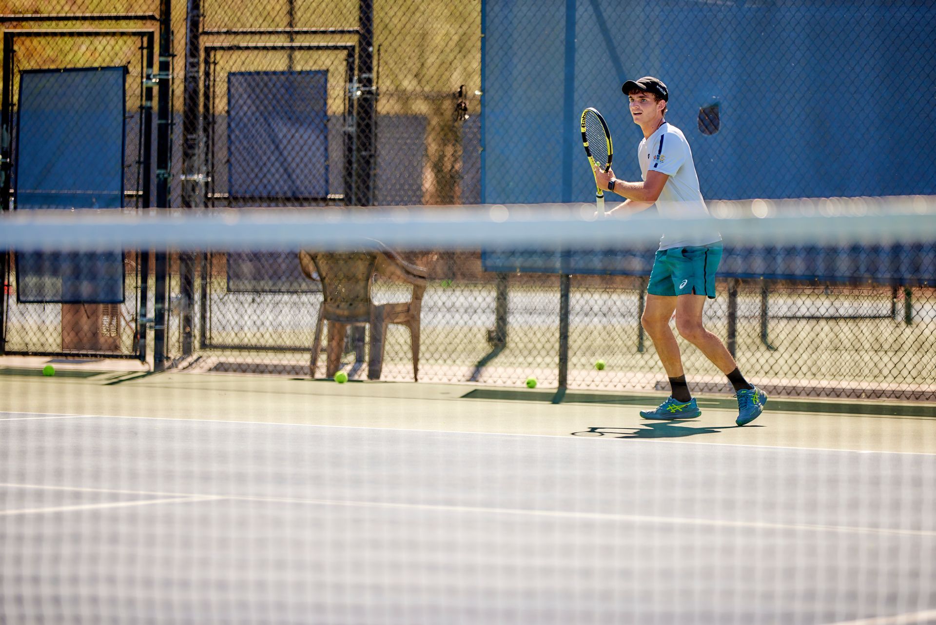 Tennis player in a blue shirt and teal shorts preparing to hit on an outdoor court.