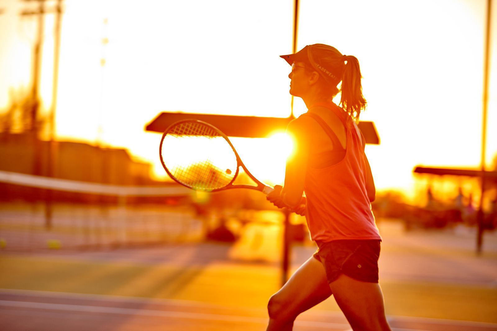 Tennis player swinging a racket on an outdoor court at sunset.