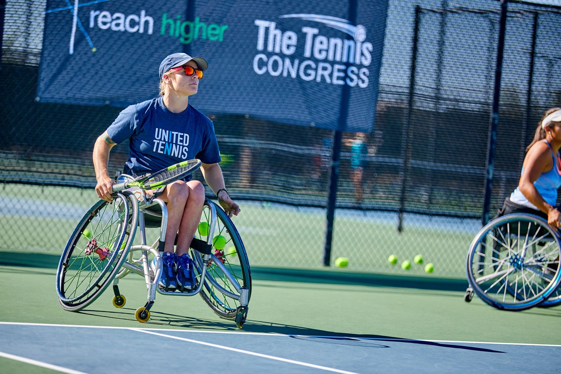 Wheelchair tennis players on a blue court. One is wearing a blue shirt, holding a racket, and looking forward.