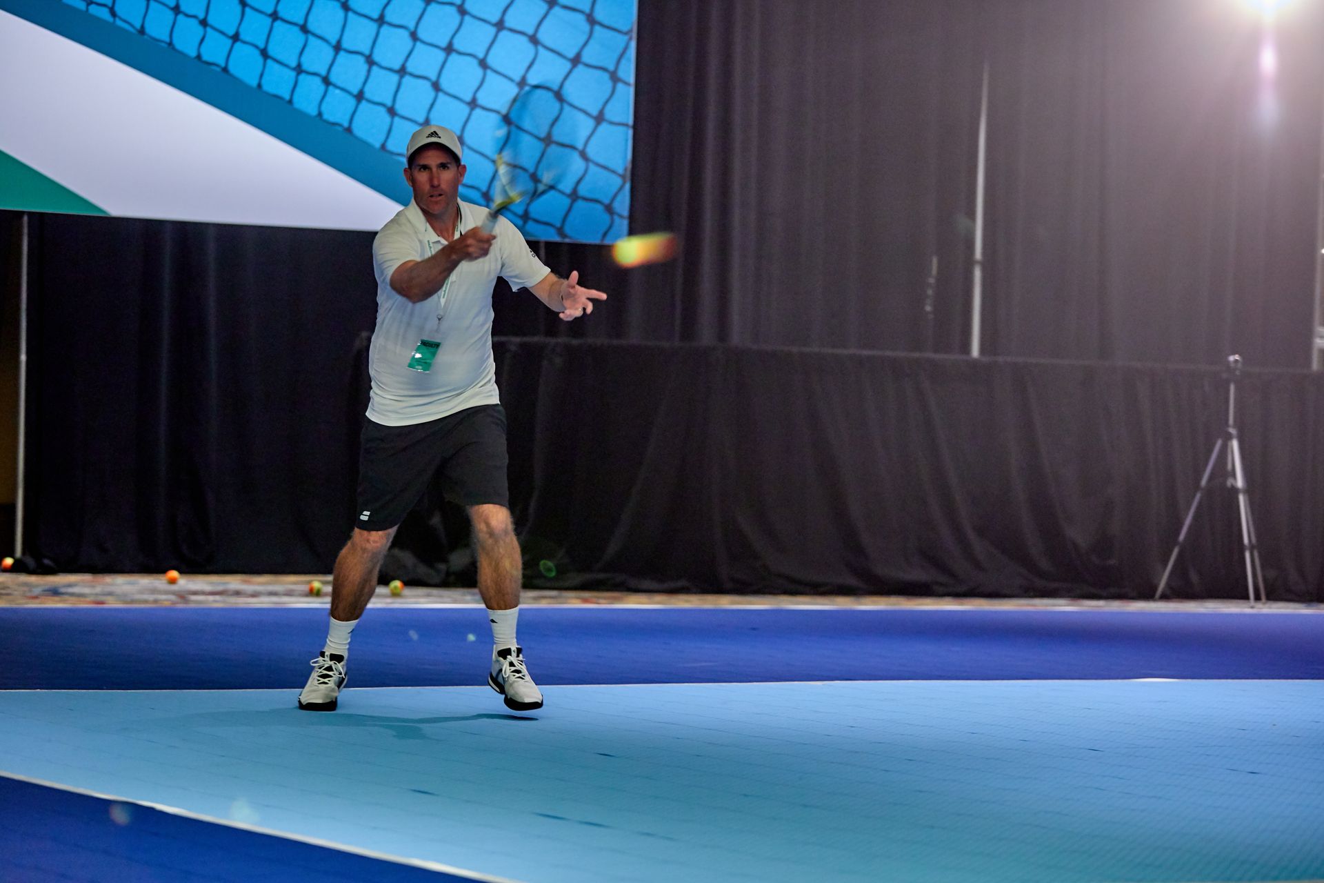 Man in tennis attire hitting a tennis ball on a blue court, with a backdrop and net.
