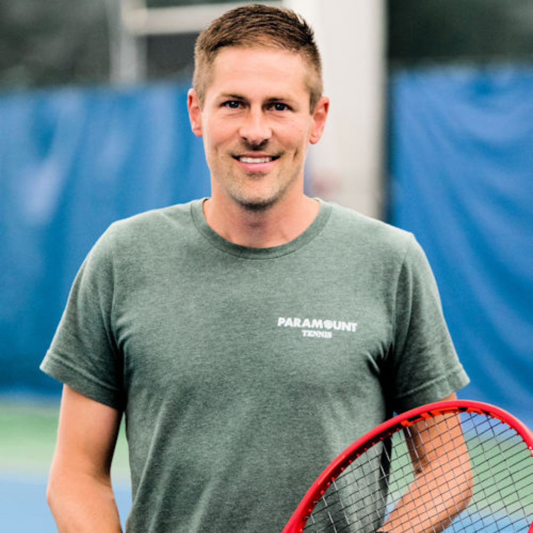 Man holding tennis racket, smiling, wearing green shirt, on tennis court.