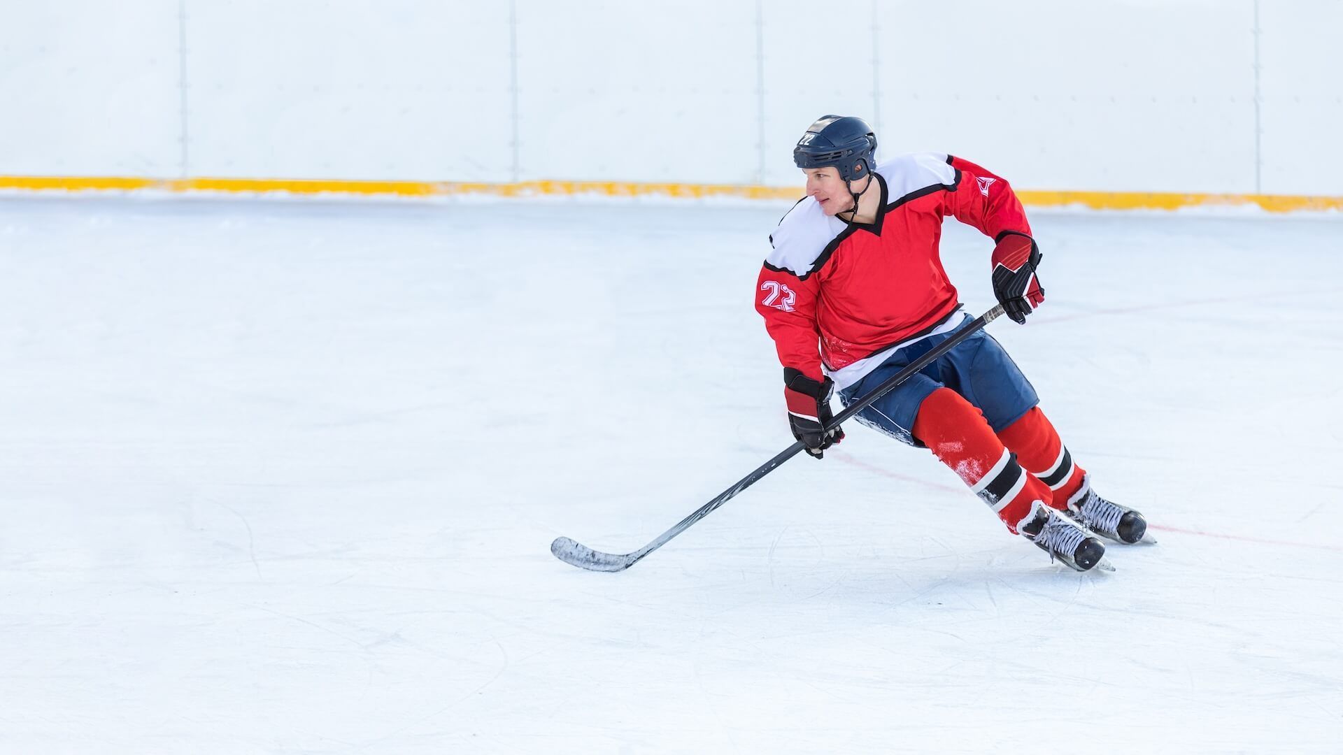 Hockey player in red jersey skating across the ice with a stick, leaning into a turn.