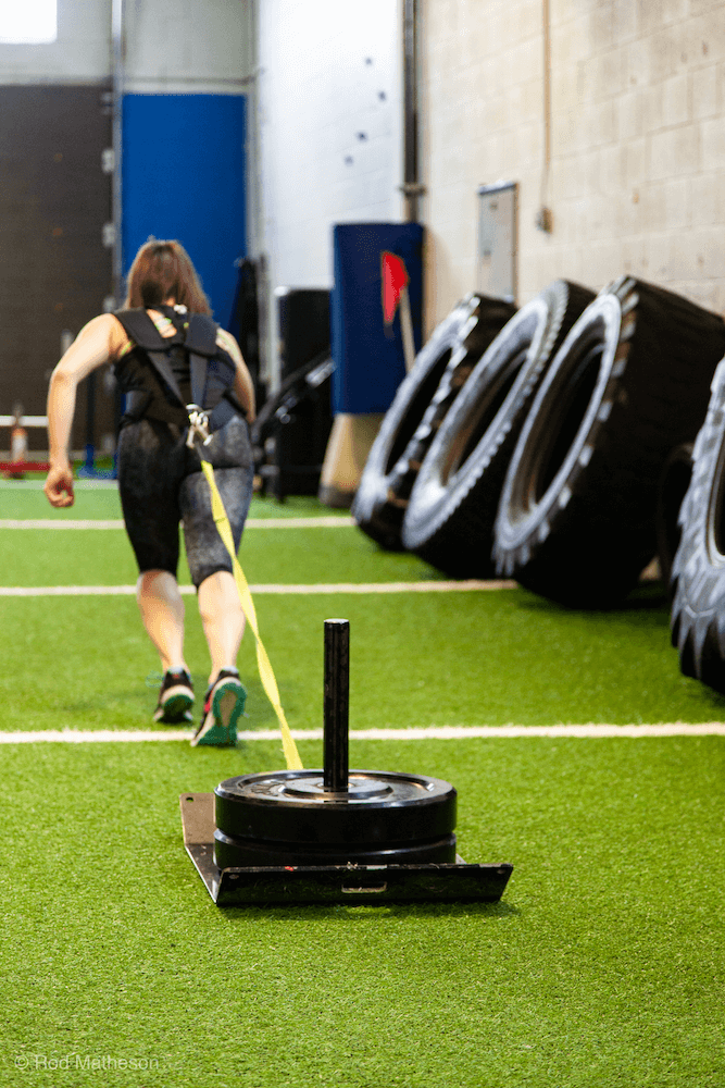 A woman is pulling a sled with a rope in a gym.