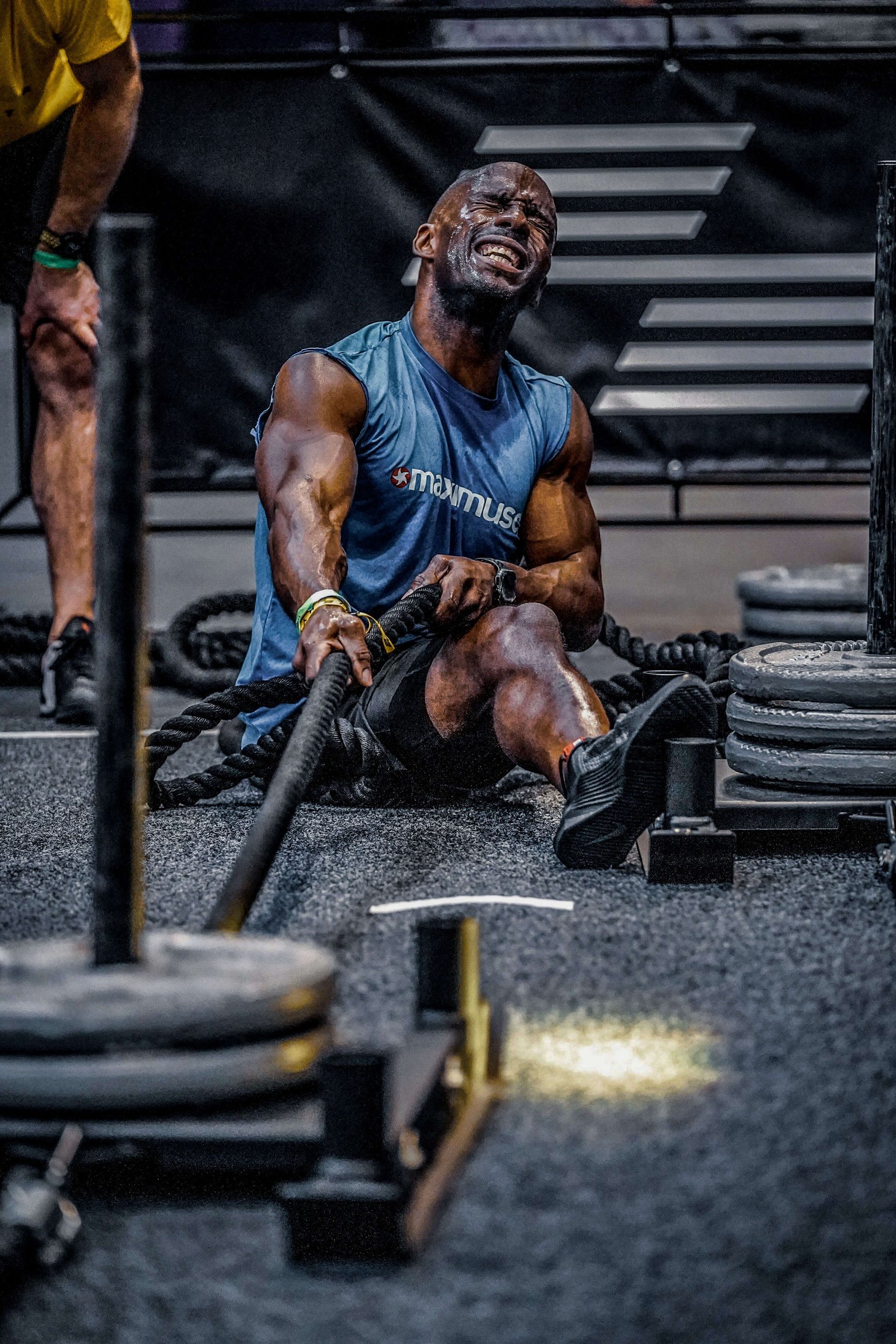 Man intensely training with a sledgehammer, sweating, at a gym.