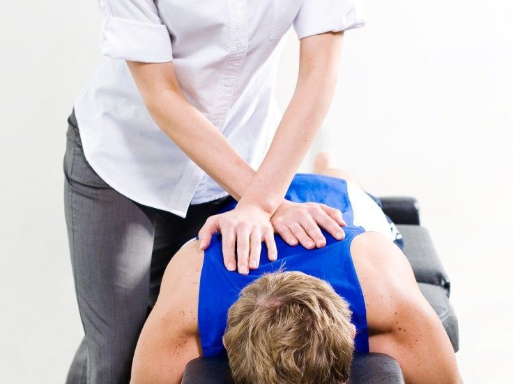 A Woman Is Giving A Man A Massage On A Table — Sea & Sand Chiropractic In Toukley, NSW