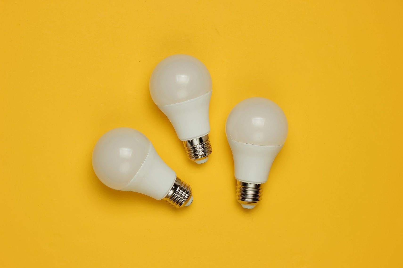Tres bombillas blancas dispuestas sobre un fondo amarillo brillante.