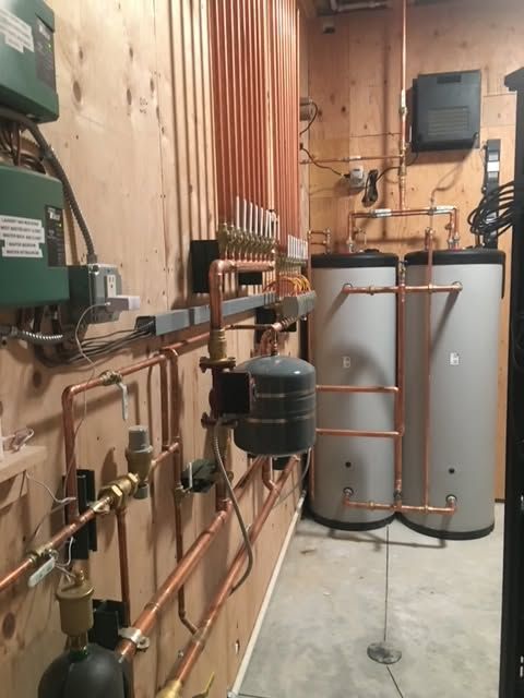 Mechanical room with copper pipes, tanks, and industrial equipment along a concrete wall