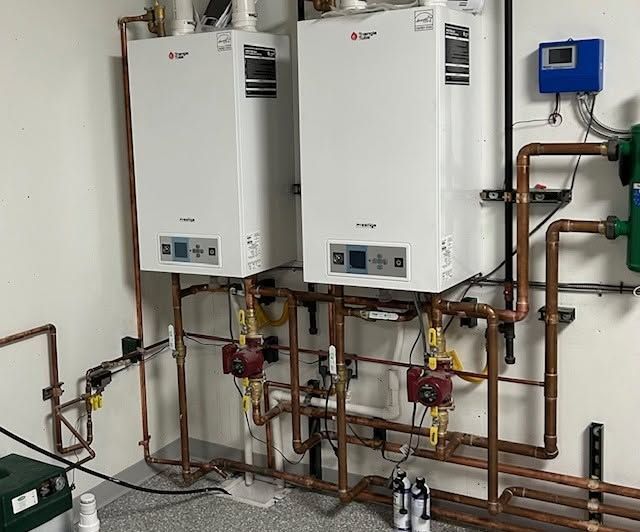 Two white wall-mounted boilers with copper piping and valves in a utility room