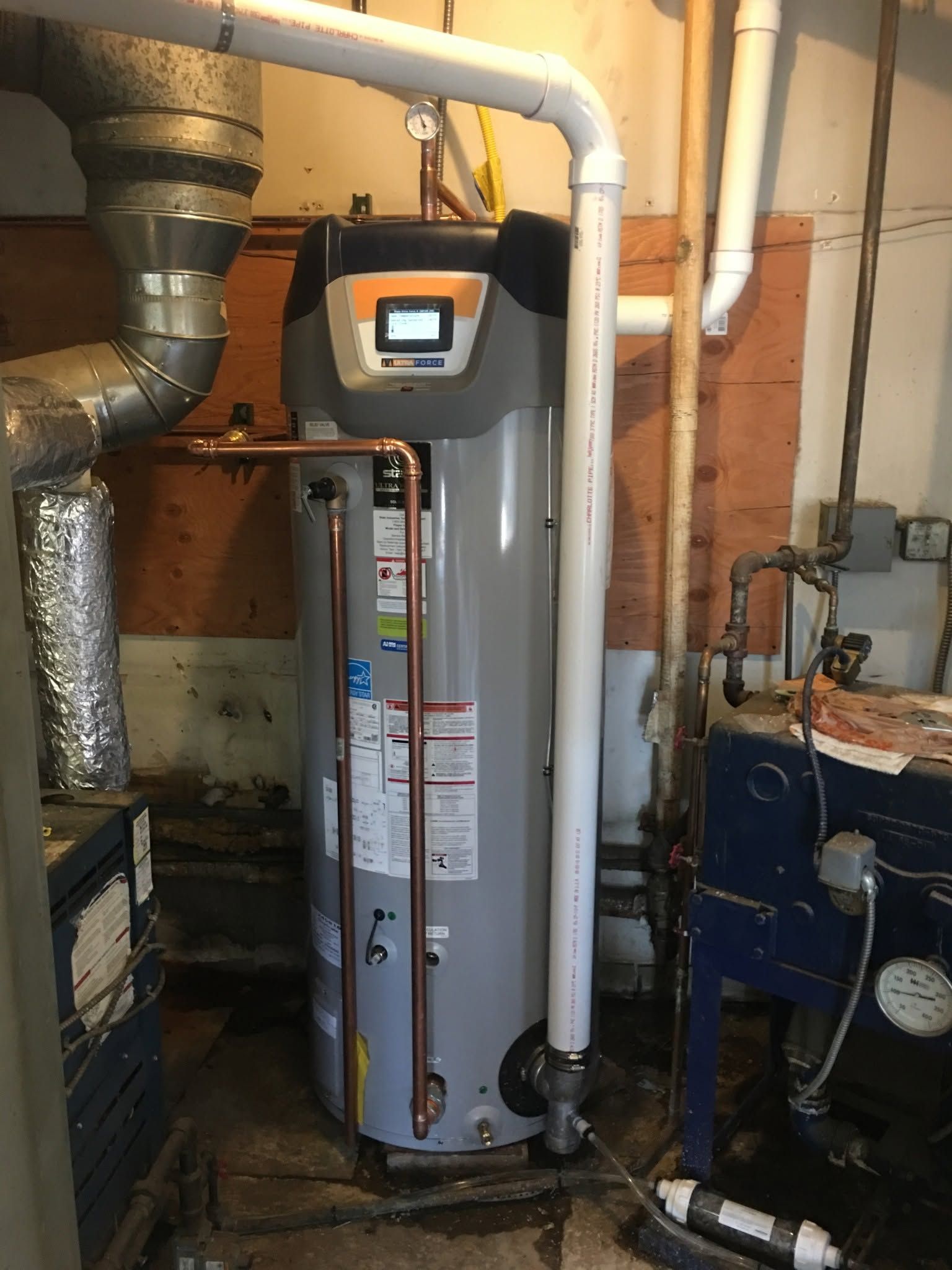 Water heater in a cramped utility room with exposed pipes and ductwork.