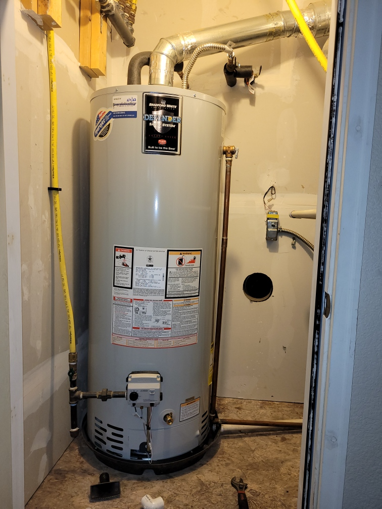 Water heater in a narrow utility closet with pipes, valves, and yellow gas line.