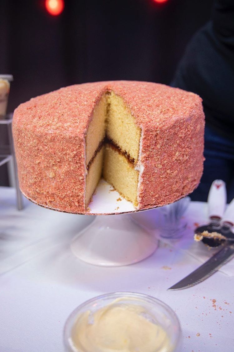 Pink-frosted layered cake with a slice removed on a cake stand at a party table