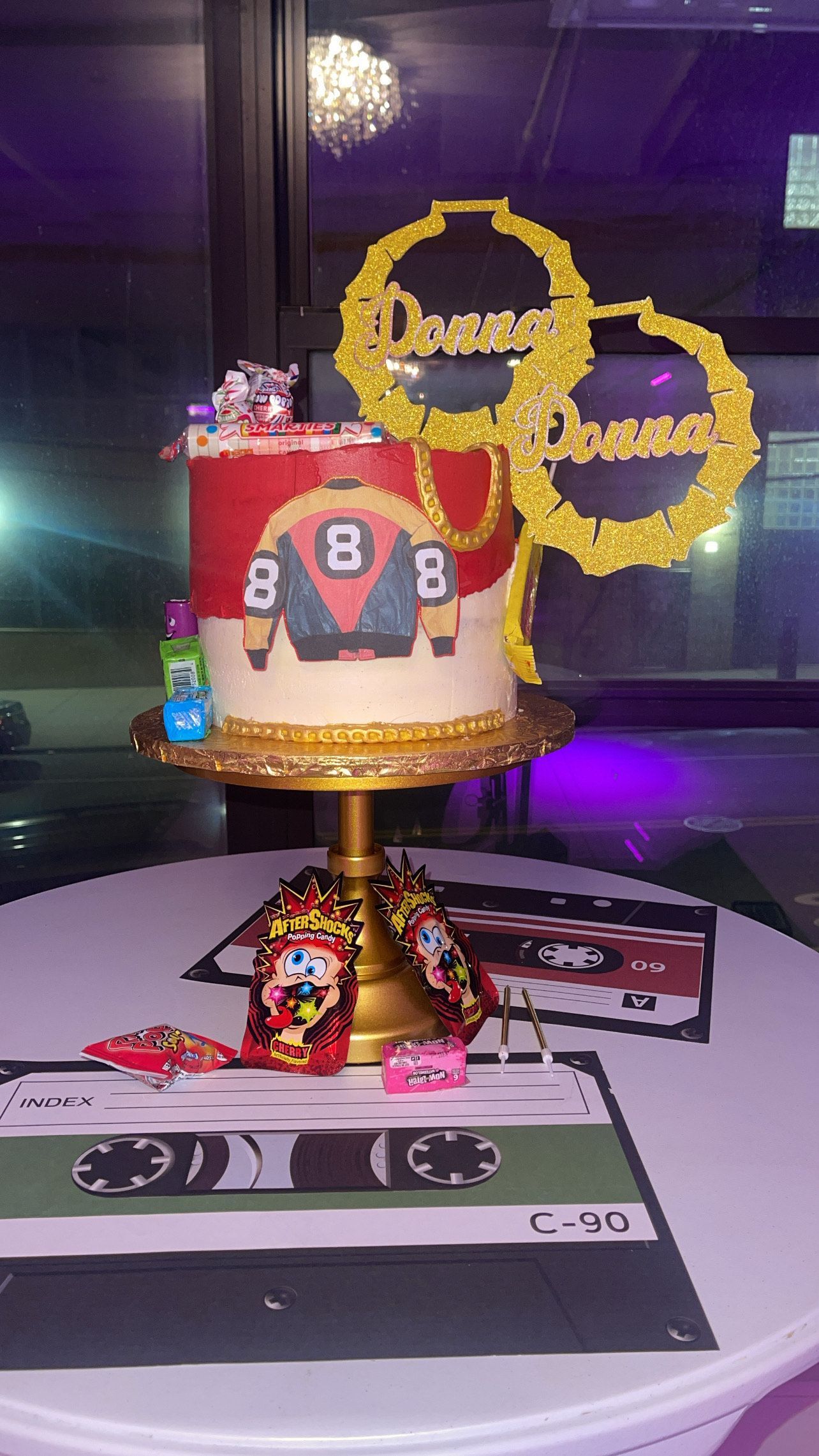 Sports-themed cake with red jersey topper and gold balloon-style number balloons on a decorated table