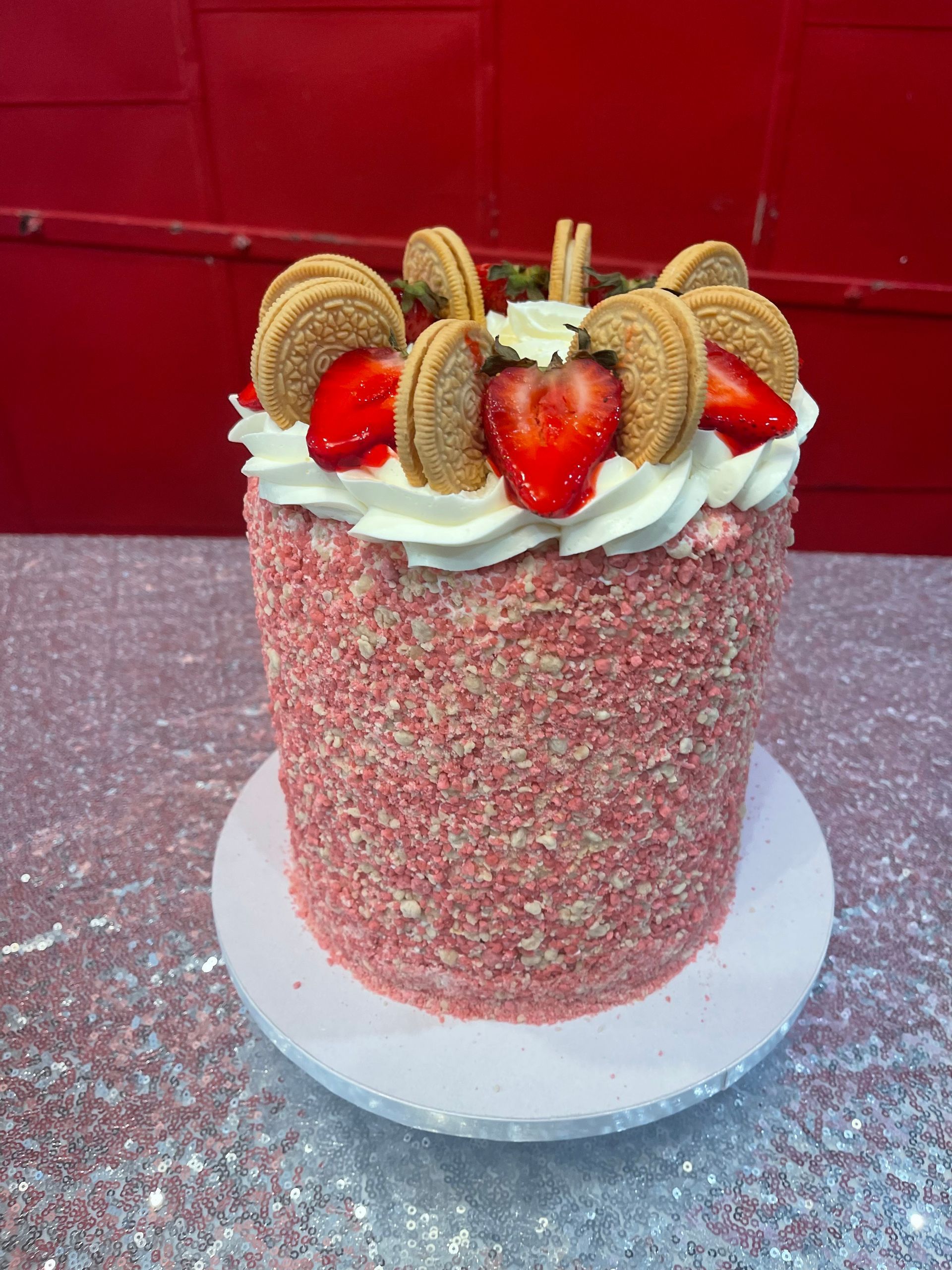 Pink cake with white frosting and strawberries, topped with cookies, on a white stand against a red background