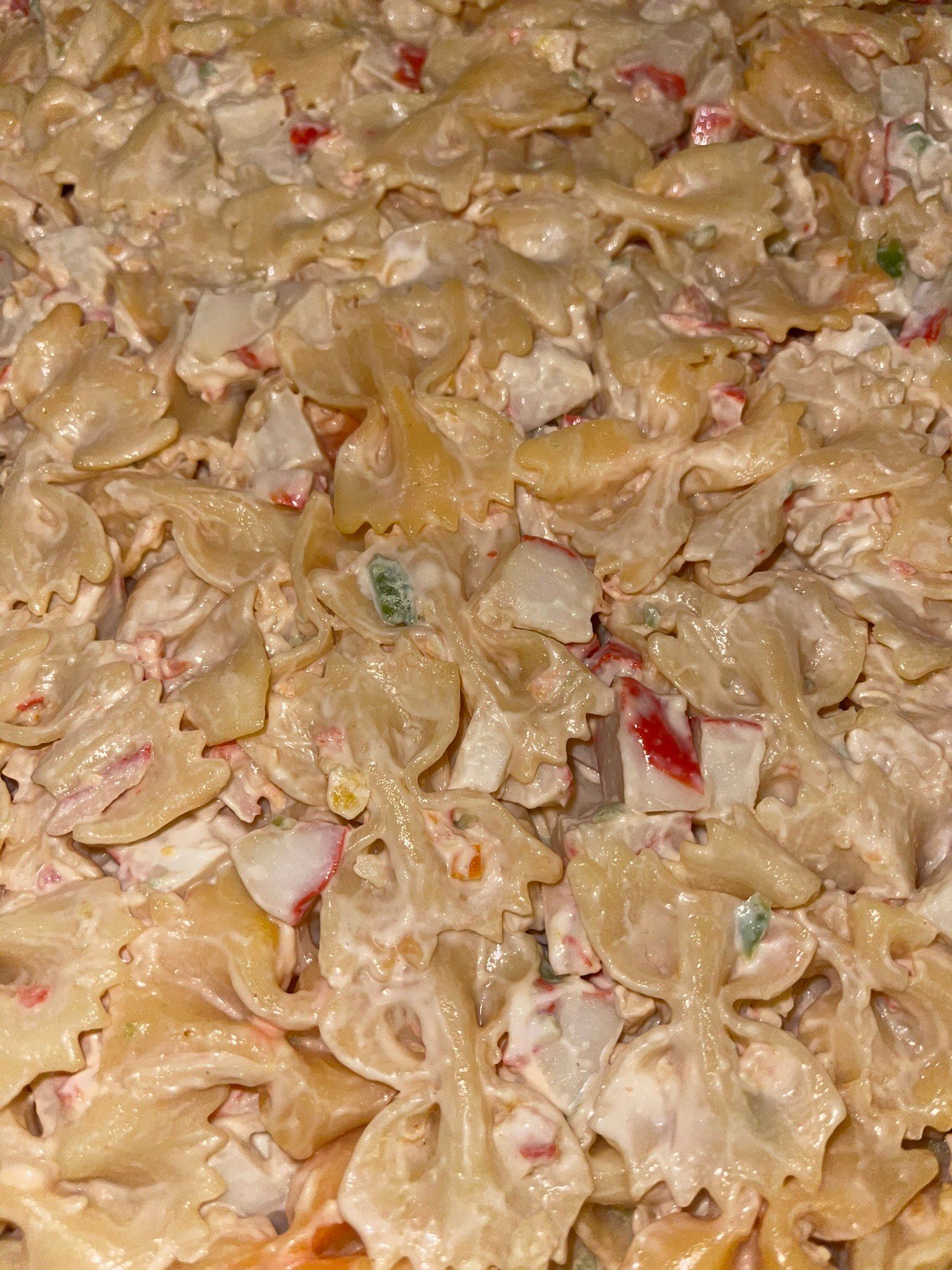Close-up of creamy pasta salad with shell noodles and small red and green vegetable pieces