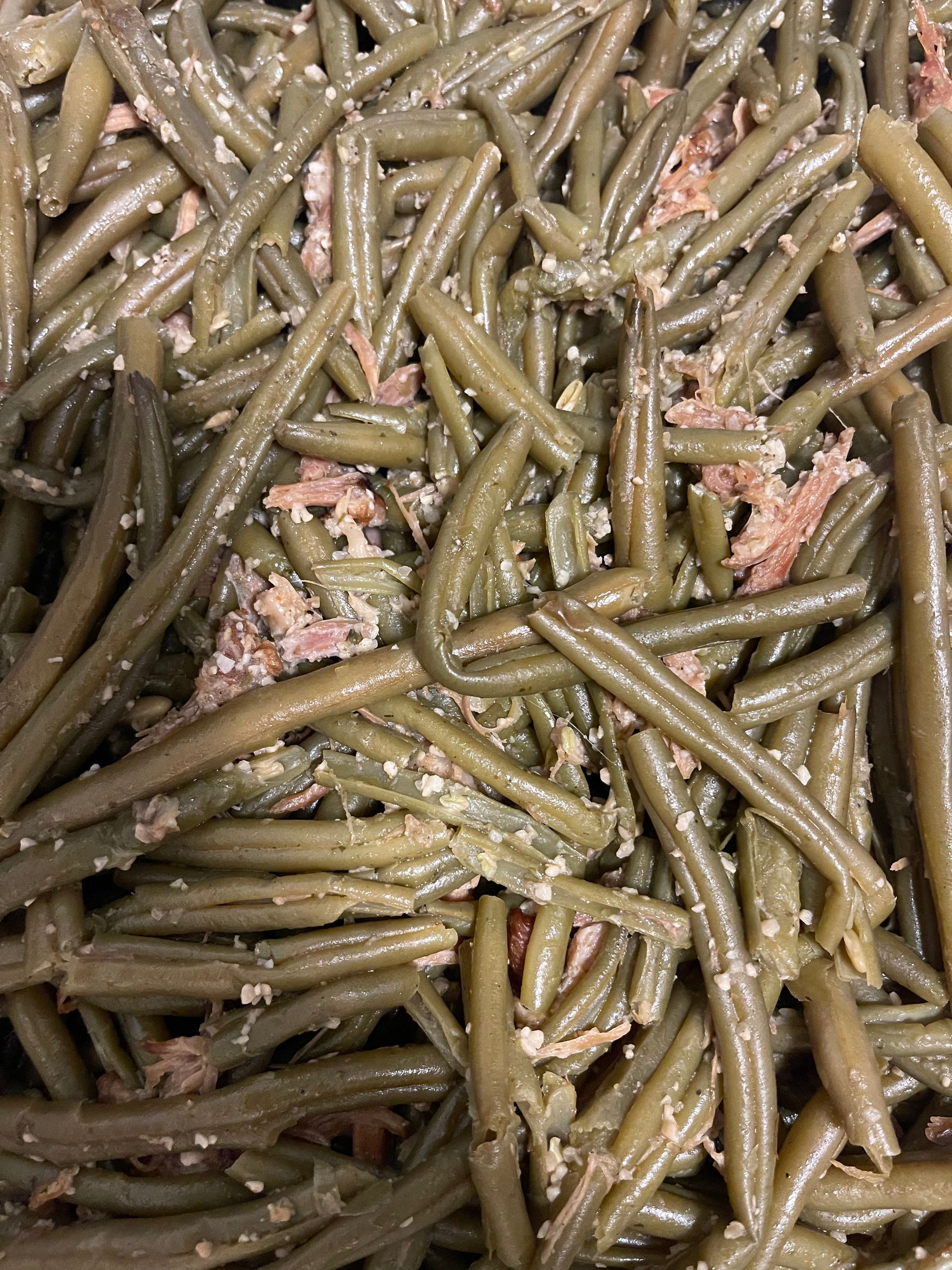 Close-up of cooked green beans mixed with rice and pink meat pieces in a dish