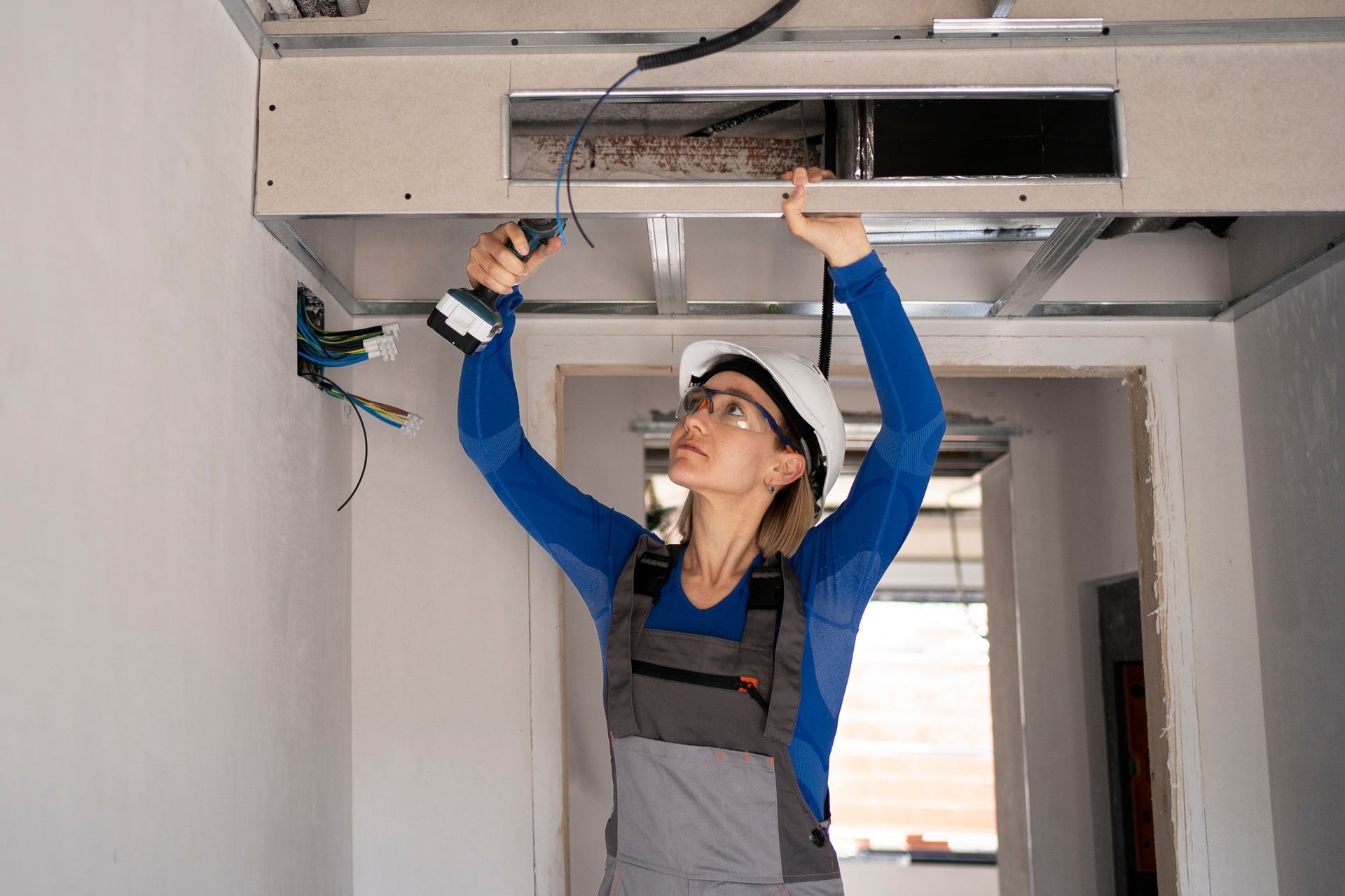 Technician inspecting ceiling HVAC ductwork with tools in a hallway
