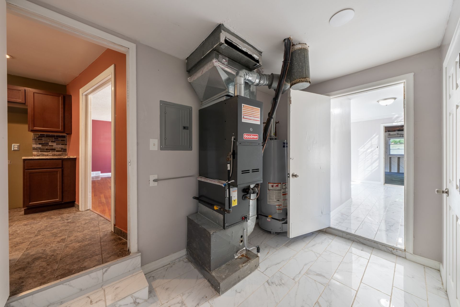 Small utility room with a furnace, white tile floor, and open door to a kitchen and another bright room