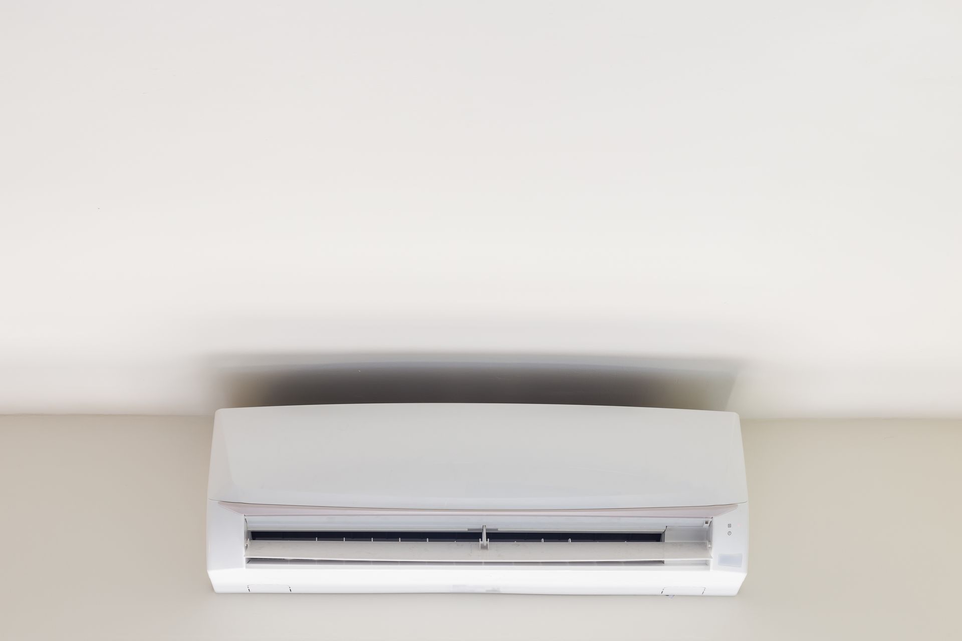 Wall-mounted white air conditioner on a beige wall, centered beneath a ceiling shadow.