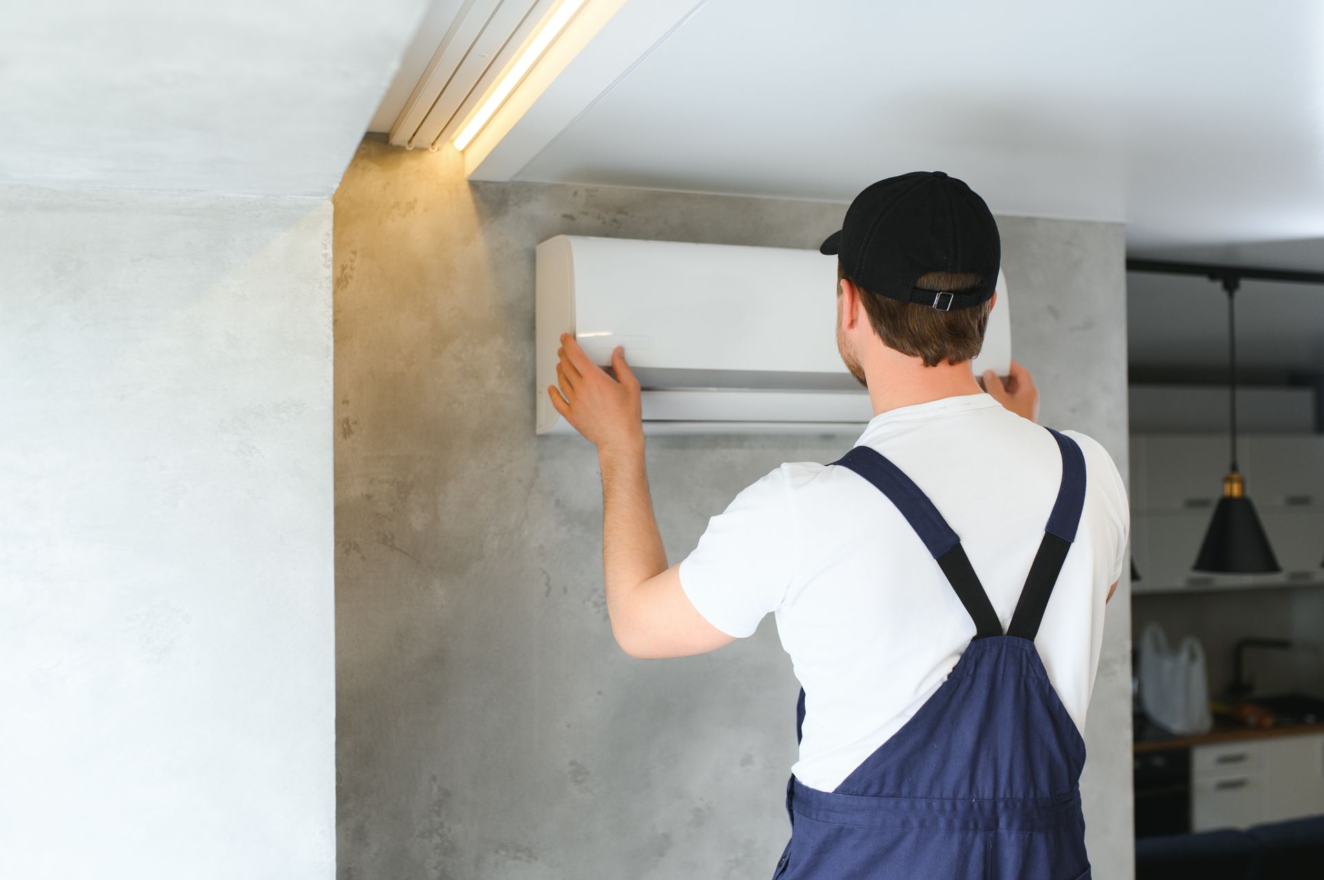 Worker in blue overalls installing a white cabinet under a ceiling light in a modern room
