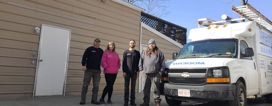 Four people standing beside a white utility van outside a beige building