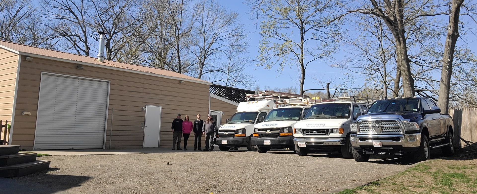 Group of people standing by white trucks outside a tan building on a gravel lot