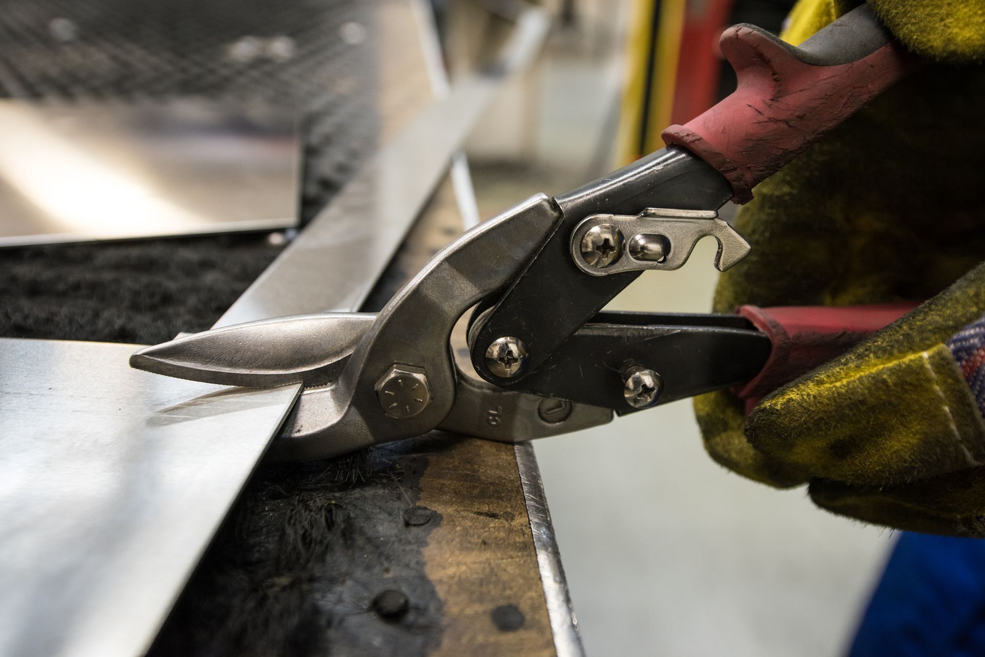 Metal shears cutting a sheet of silver metal on a workbench