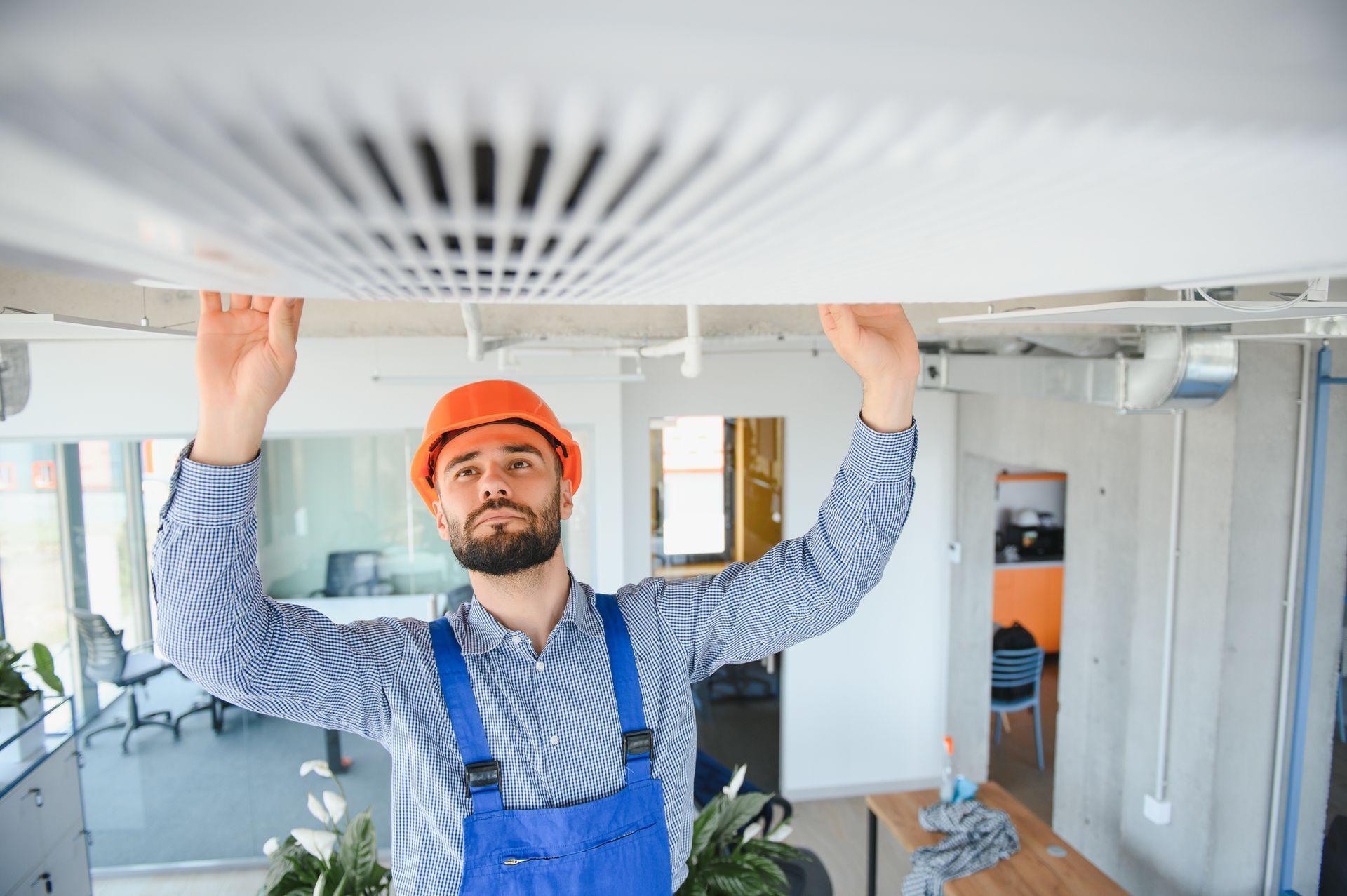 A man wearing a hard hat and overalls is working on a ceiling.