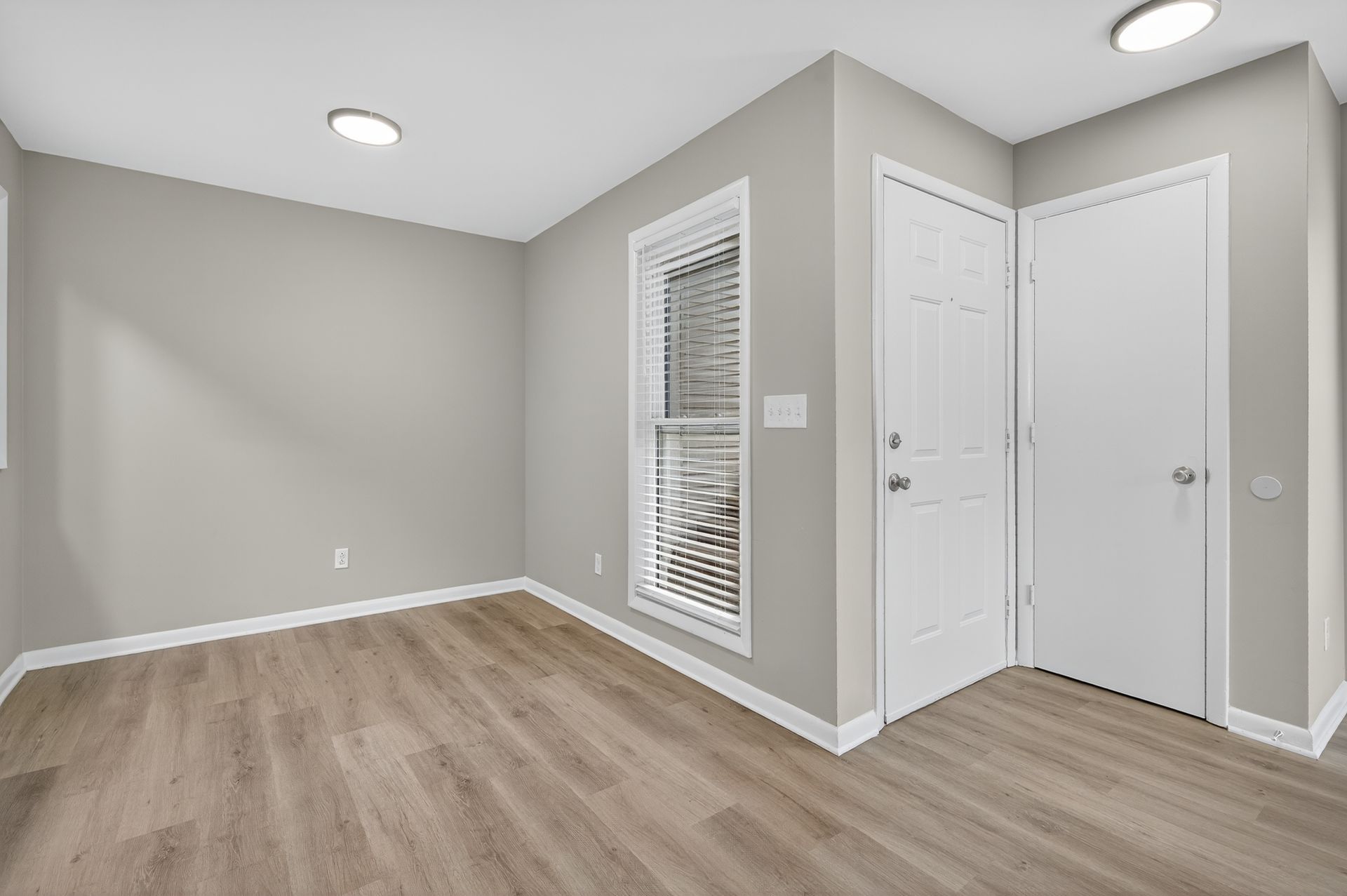 Empty beige room with wood flooring, white trim, recessed lights, window blinds, and double closet doors